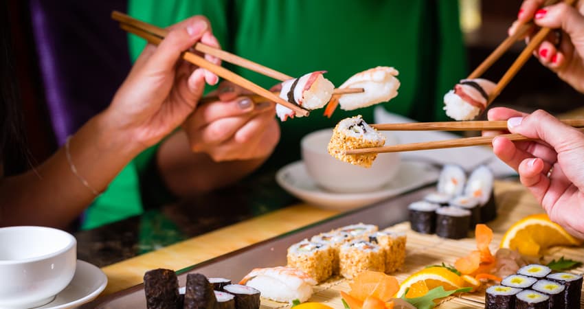 A group of people holding sushi with chopsticks at a restaurant 