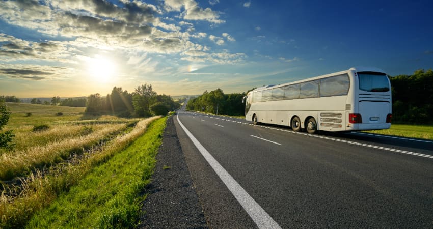 A charter bus drives into the sunset on an empty freeway