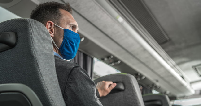 A man in a suit wears a mask while traveling on a charter bus