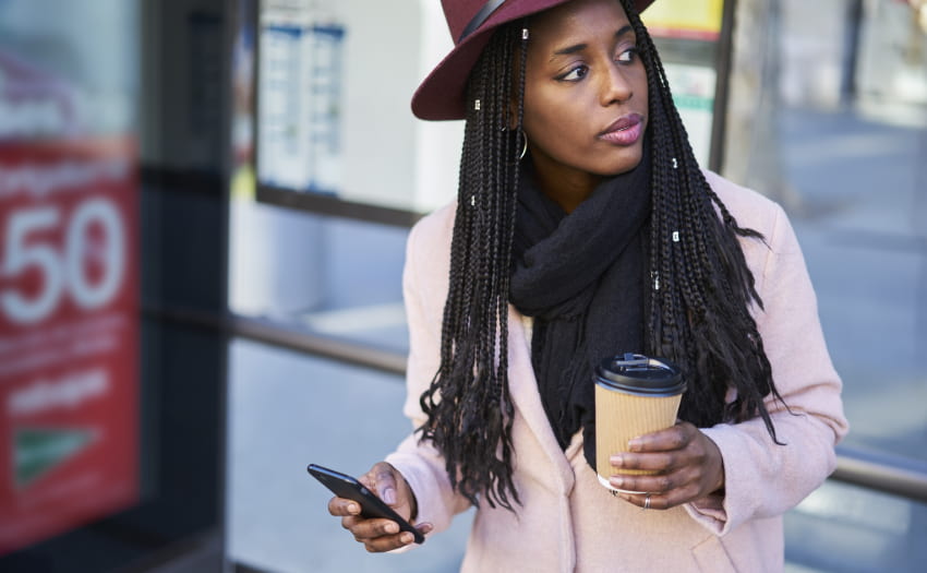 A woman stands at a bus station with her coffee as she commutes to work