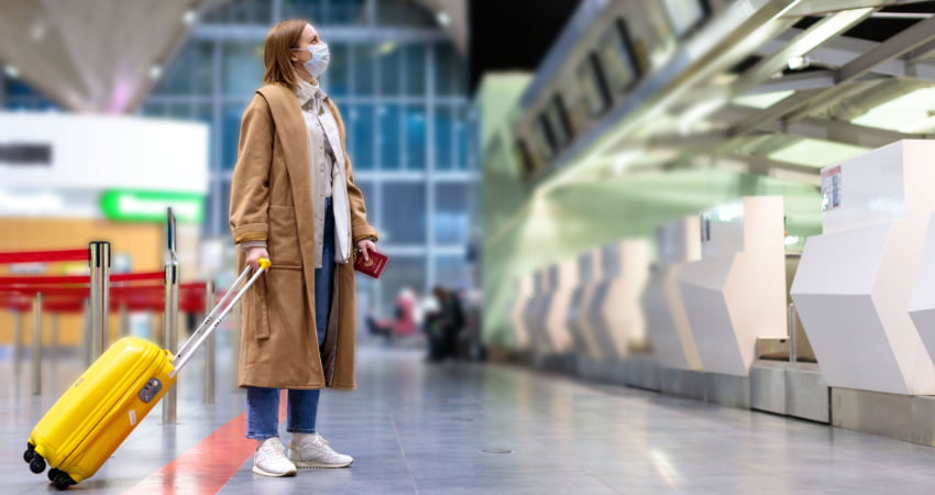 A lone woman in a mask stands at a ticket counter in an airport