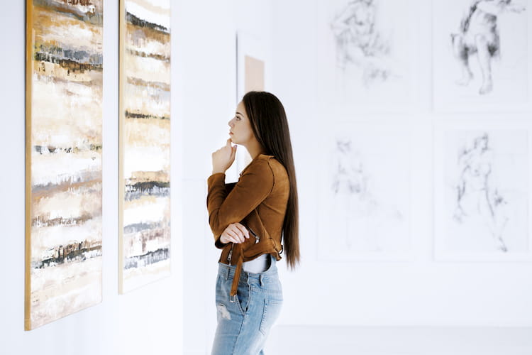 a woman looks at a gallery painting and thinks