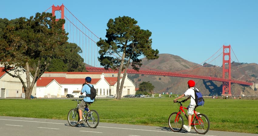 Two bikers ride past a viewpoint of the Golden Gate Bridge in the Presidio