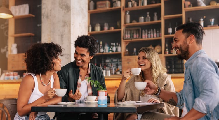 friends laugh and hold coffee cups at a table in a cafe