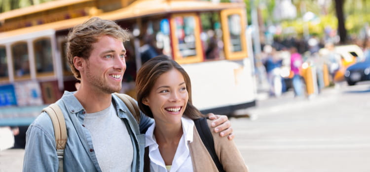 a couple smile while standing on a san francisco street with a cable car in the background
