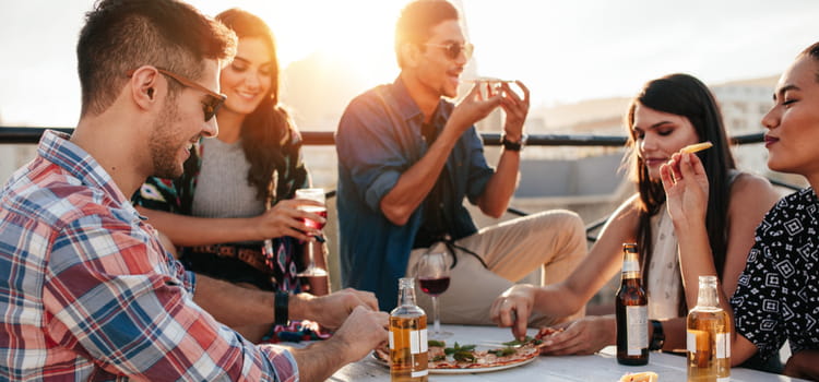 a group of friends sits at a seaside table while enjoying appetizers and drinks