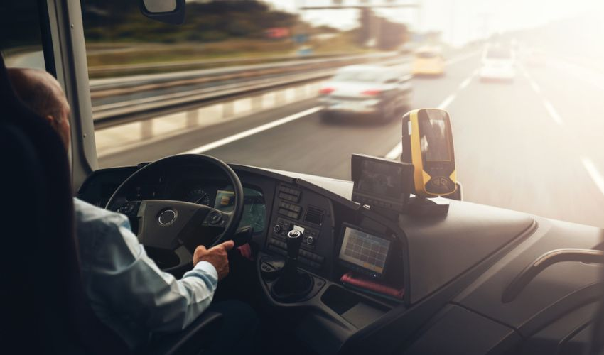 A bus driver behind the wheel of a charter bus looking through the front windshield at the highway road.