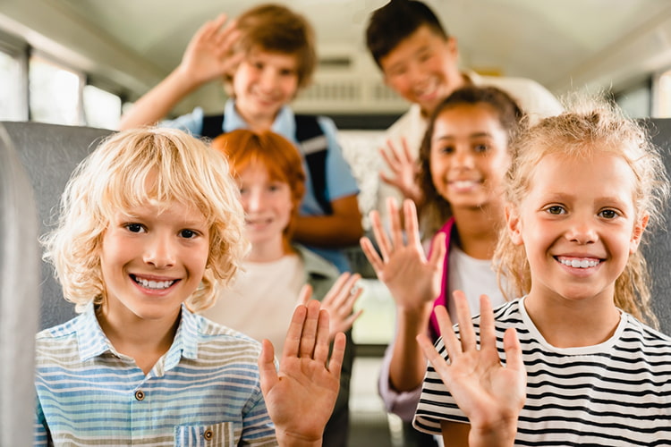 kids on a bus smiling and raising their hands