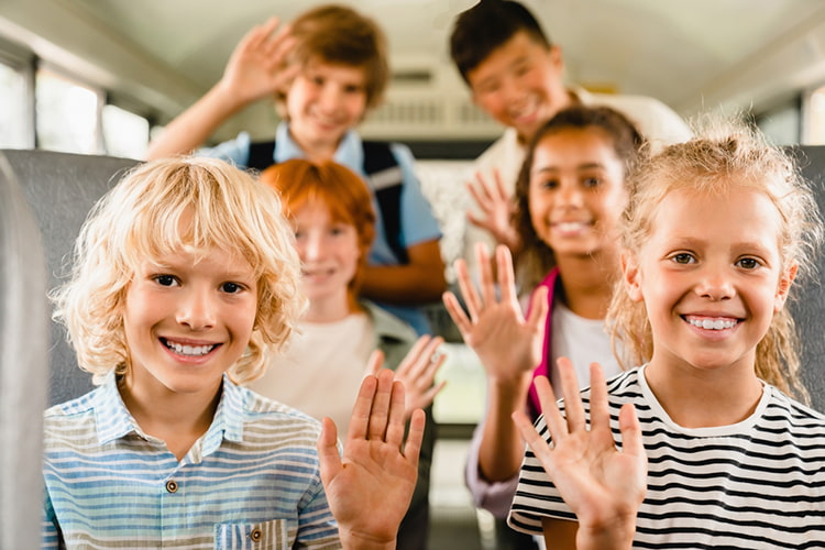 kids on a bus smiling and raising their hands